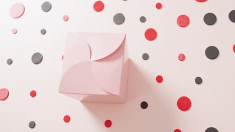 overhead view of pink gift box on white background with red and black dots