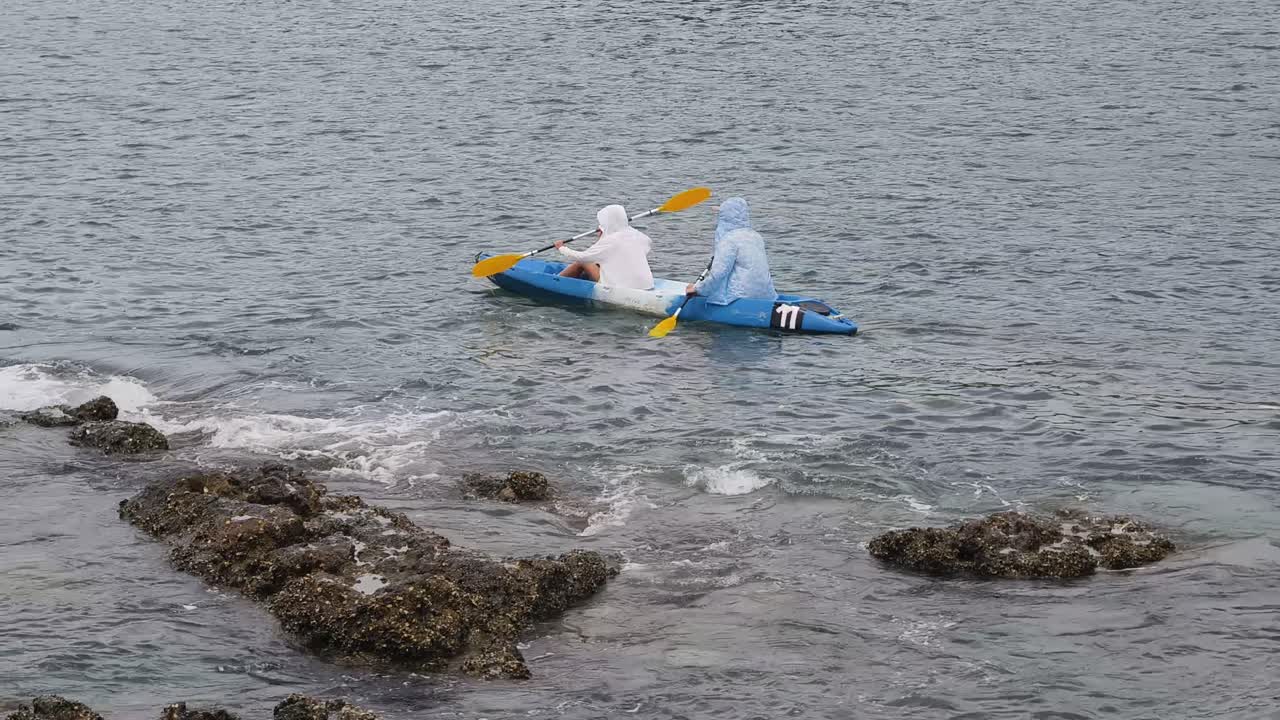 Two people kayaking in the ocean near the shore