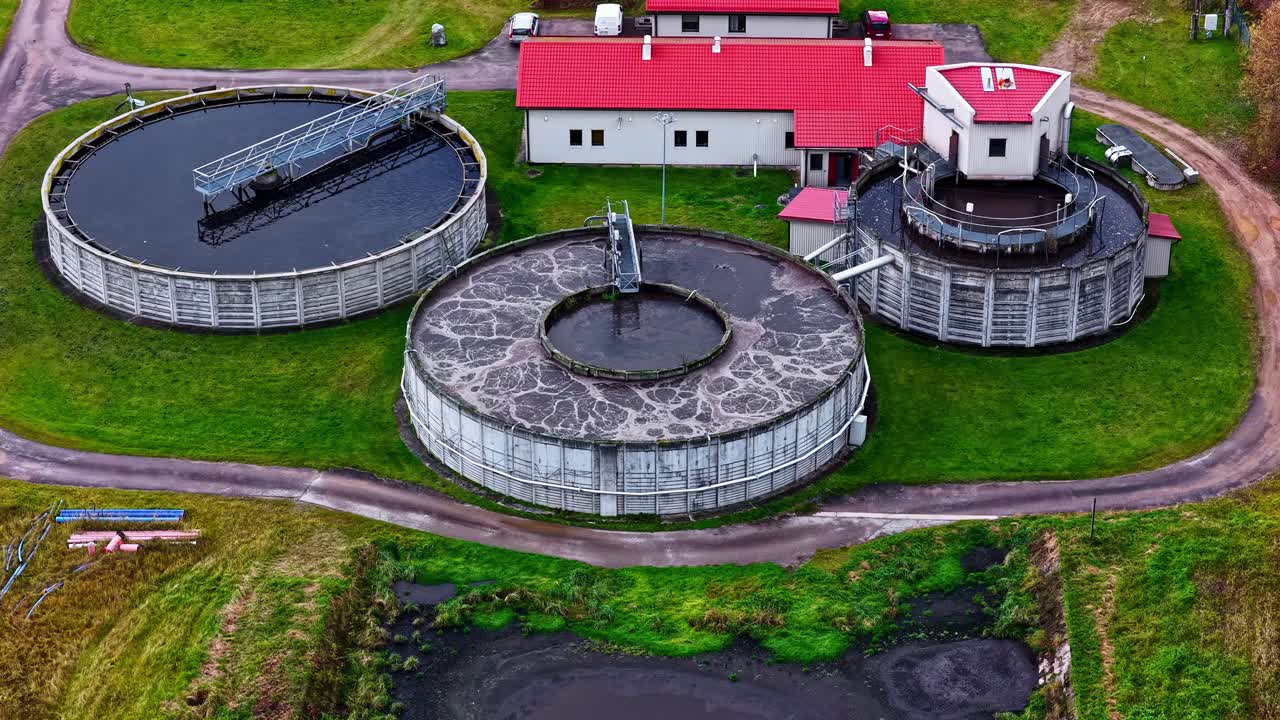 Circular waste water treatment plant tanks sit beside red building with clear geometric layout