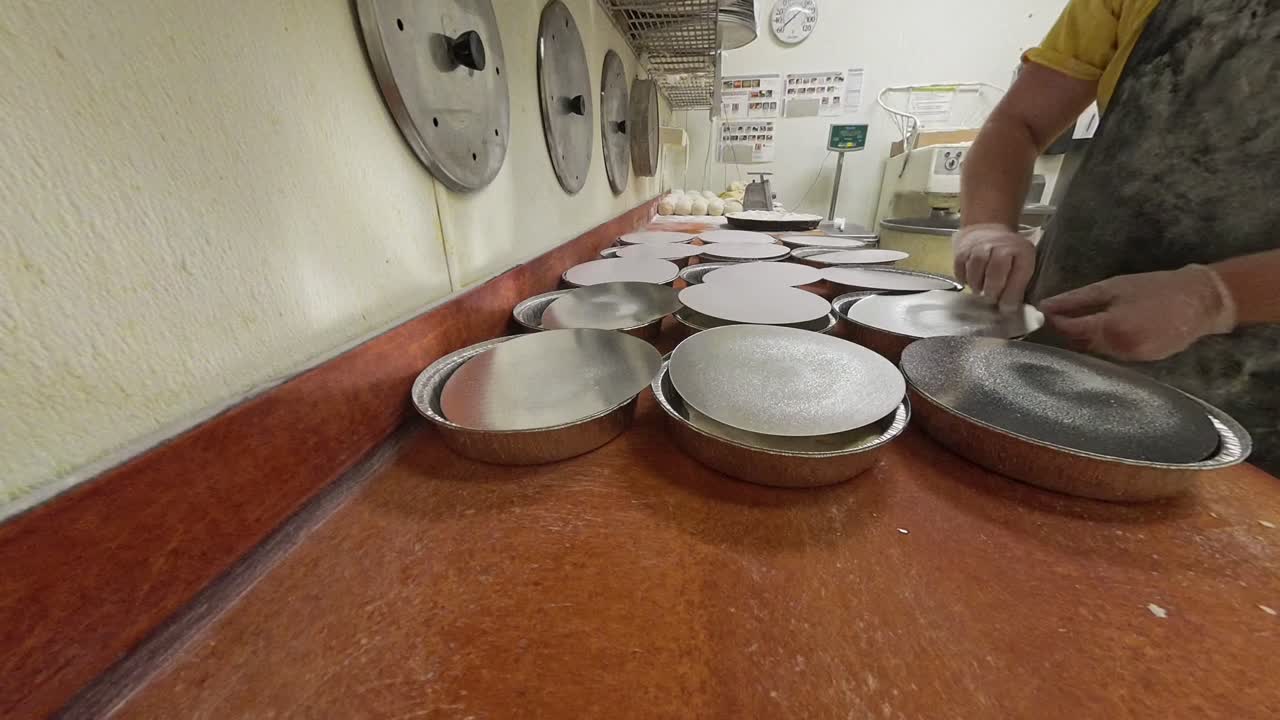 Worker flipping oiled lids for aluminum foil with pizza dough.