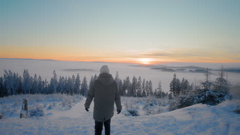 turista viendo la puesta de sol dorada en un mirador en un sendero en las montañas en una fría noche de invierno