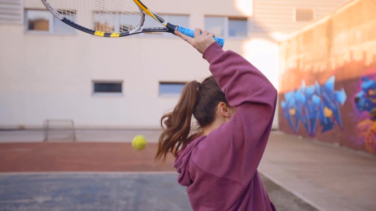 젊은 여성이 다채로운 도시 테니스 코트에서 테니스를 배우고 있습니다.