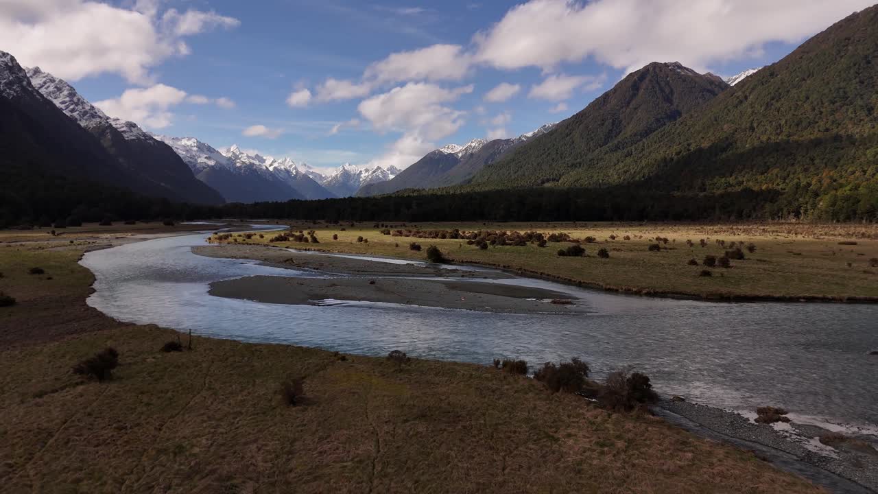 Riprese cinematografiche con drone a bassa quota del fiume Eglinton che scorre attraverso una vasta valle tra cime innevate sulla strada per Milford Sound, Southland, Nuova Zelanda