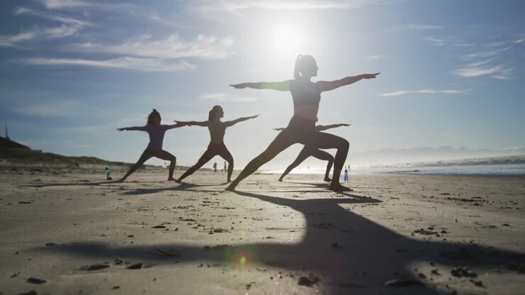 Gruppo di amiche donne di diverse etnie che praticano yoga in spiaggia