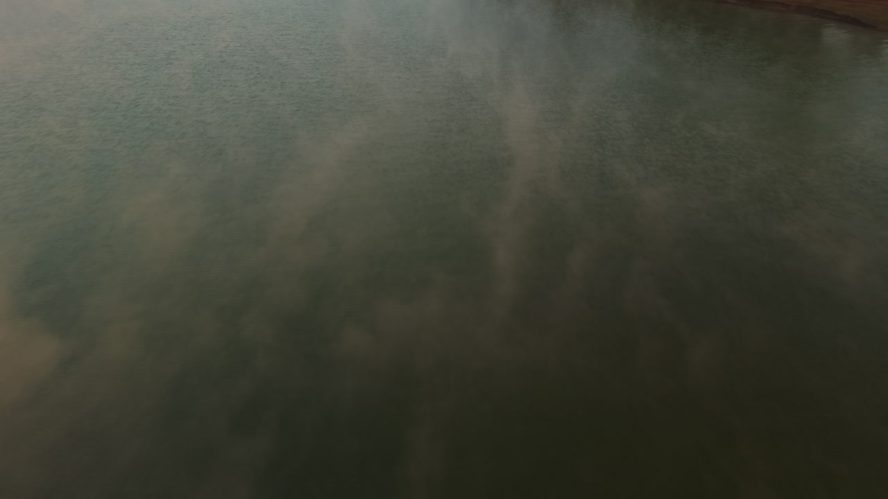 Early morning mist moving softly over a still, dark green lake surface