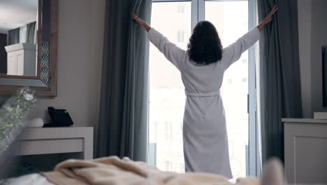 woman opening curtains in a hotel room