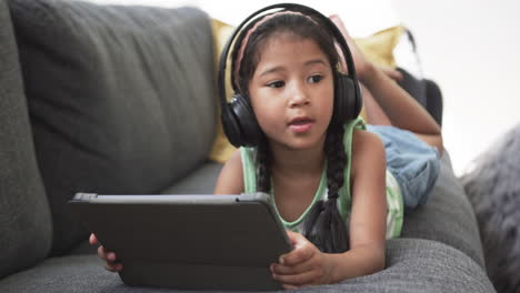 una chica biracial con el cabello trenzado que usa auriculares usa una tableta