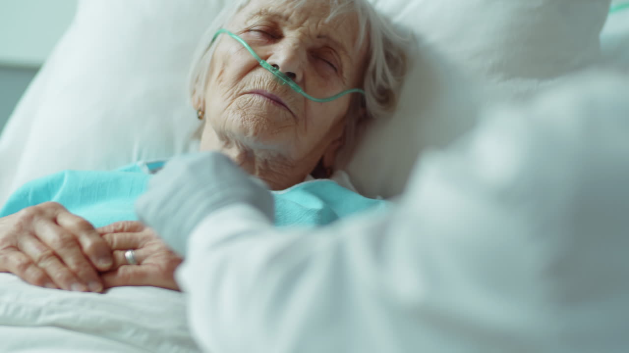 Medico che tiene la mano di un paziente anziano incosciente