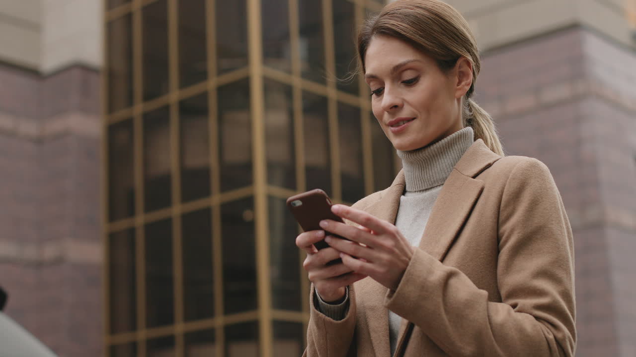 вид снизу на кавказскую деловую женщину в элегантной одежде, набирающую текст на смартфоне на улице осенью