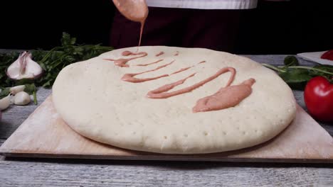 chef preparing pizza with tomato sauce