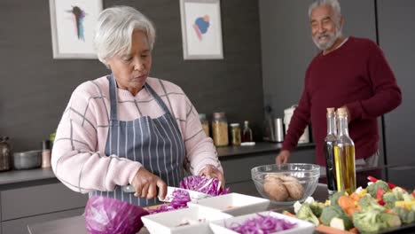 Senior-biracial-couple-cooking-dinner-and-chopping-vegetables-in-kitchen,-unaltered,-in-slow-motion