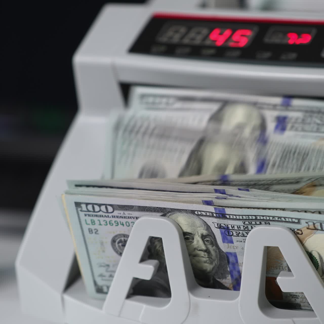 Cash counting machine switched on and the rollers begin to rotate. A wad of hundred dollar notes are placed into machine to be counted. Close up