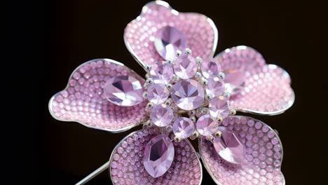 delicate pink flower brooch adorned with glittering crystals rotating gracefully, revealing intricate design and sparkling elegance against dark sophisticated background