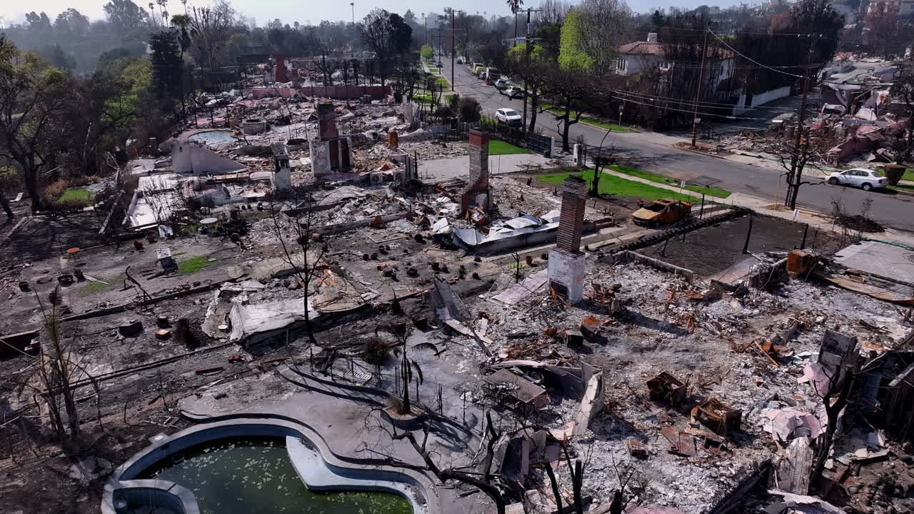 Aerial view of a residential neighborhood devastated by a wildfire, showing widespread destruction and rubble
