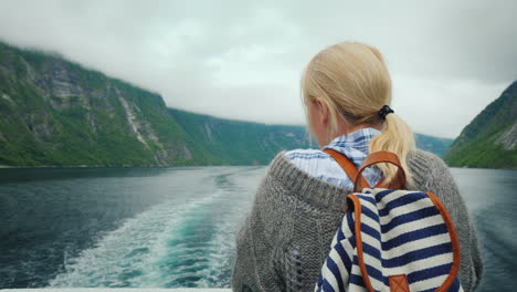 a woman stands at the stern of a cruise ship looks at the retreating rocks and waves of the fjord