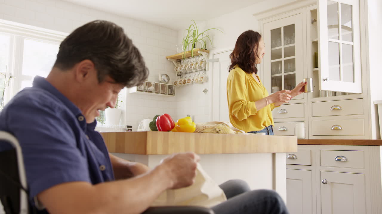 ⁇ 체어에 앉은 남편과 함께 성숙한 아시아 커플이 쇼핑 여행 후 부 ⁇ 에서 신선한 제품을 풀고 있습니다. 느린 속도로 촬영되었습니다.