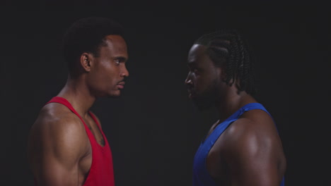 Close-Up-Of-Two-Male-Boxers-Going-Face-To-Face-Before-Boxing-Match-Staring-At-Opponent-In-Profile-Against-Black-Background