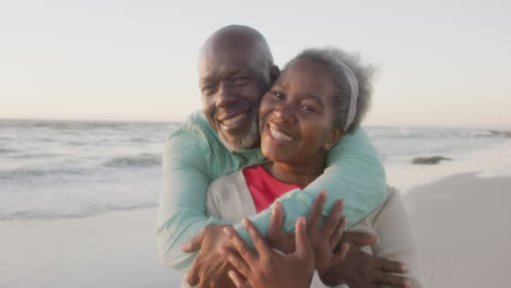 Portrait-of-happy-senior-african-american-couple-embracing-at-beach,-in-slow-motion