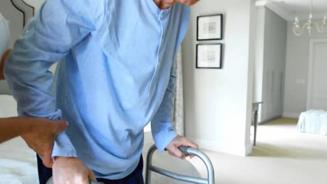 senior woman helping senior man to walk with walker in bedroom