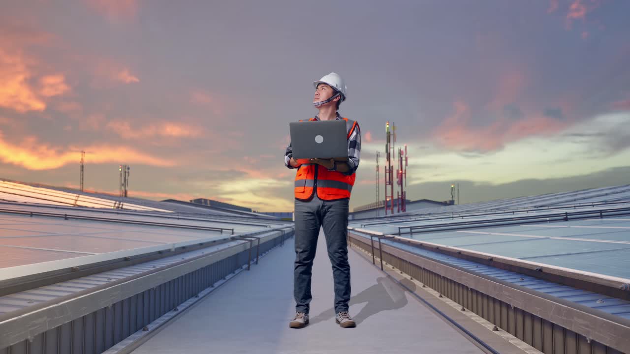 Full Body Of Asian Male Engineer With Safety Helmet Working On A Laptop And Looking Around While Standing and Inspecting Solar Panels on Rooftop