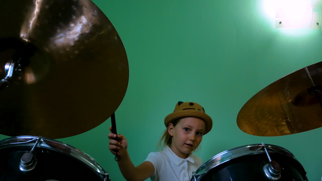 niño estudiando batería en la escuela de música. kit de batería negra. pequeño músico baterista con pinceles de batería entrenando en el fondo de la pared verde. niña rubia con sombrero jugando y sonriendo en la lección. 4k