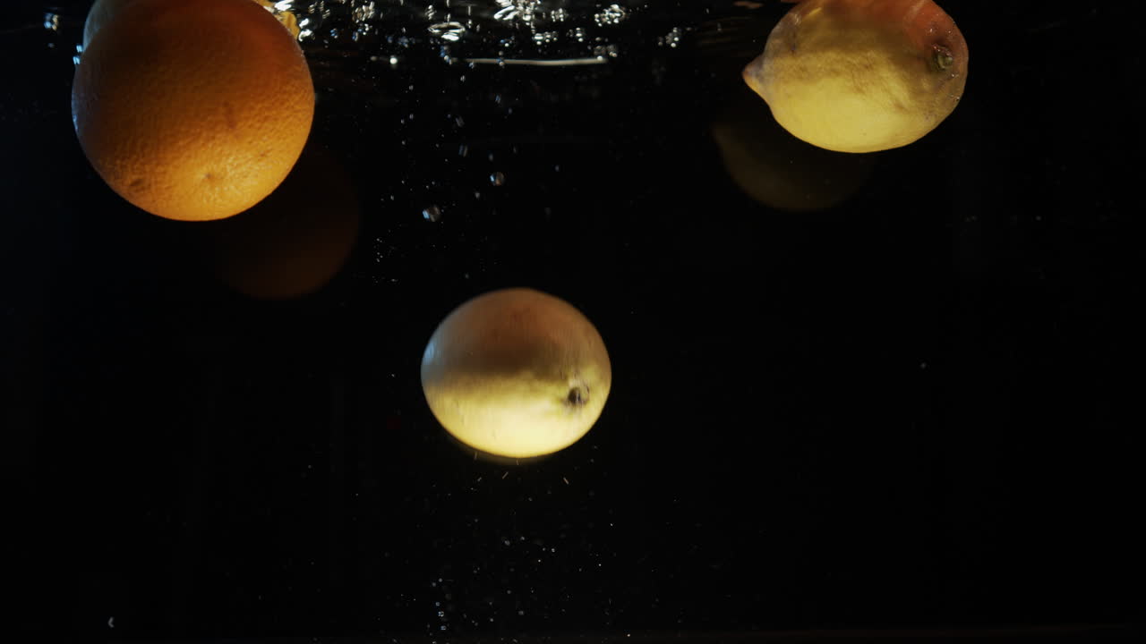 Lemons and oranges falling into water slow motion