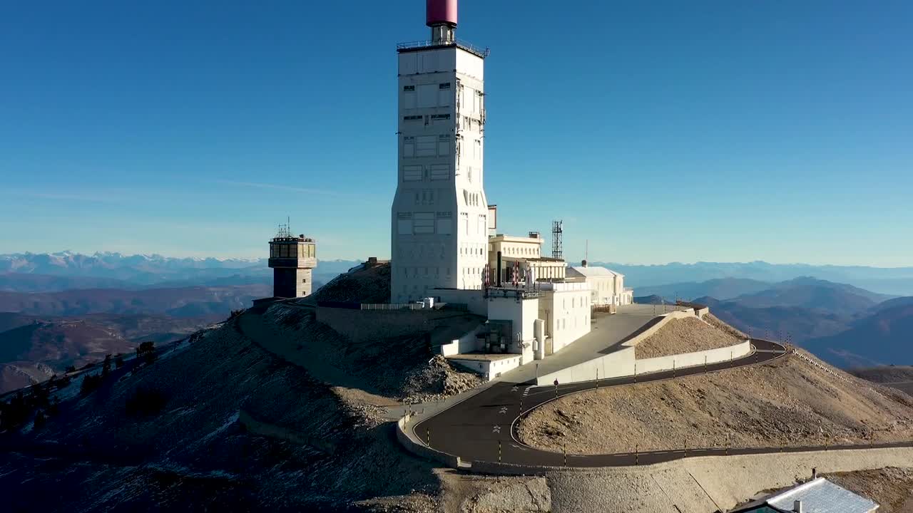 Aerial drone tilt up footage of summit observatory and winding road on Mont Ventoux in Provence France showing mountain peak structure, vast rocky terrain, and panoramic alpine landscape