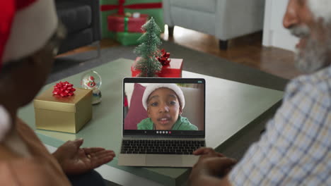 feliz pareja afroamericana senior en videollamada en portátil con su nieto en tiempo de navidad