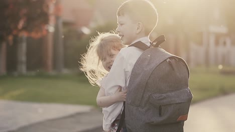 Cu-Zeitlupenporträt-Eines-Schuljungen-Mit-Rucksack-Auf-Dem-Rücken-In-Schuluniform,-Er-Hält-Ein-Kleines-Mädchen-In-Seinen-Armen