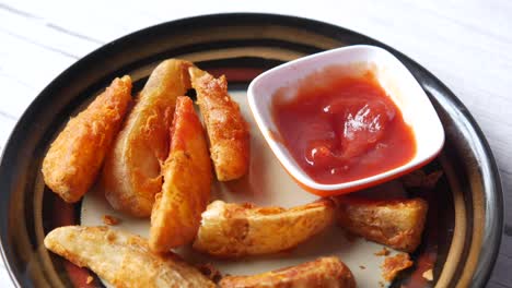 hand dipping potato wedges in ketchup