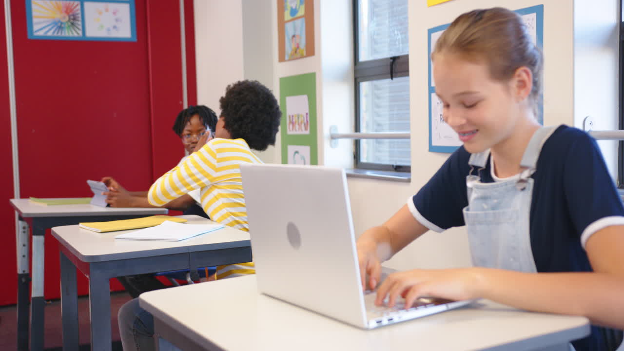 In school, girl using laptop while classmates talking in classroom