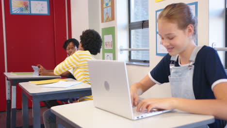 in school, girl using laptop while classmates talking in classroom