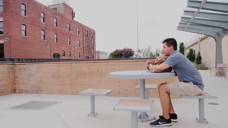 wide view of young, male adult sitting and contemplating at public park table in bricktown, oklahoma city, usa. -static sho