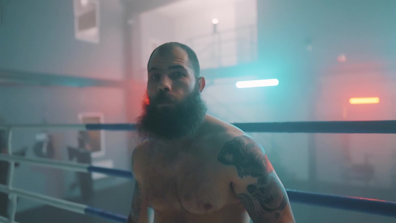 Intenso pugile barbuto in piedi in un ring da boxe dall'atmosfera drammatica