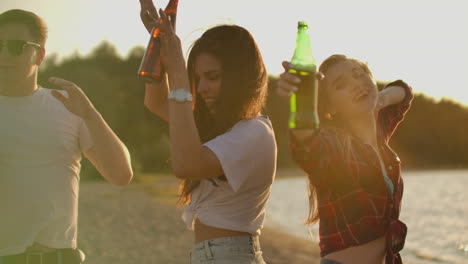 two girls are dancing in short t-shirts with beer on the beach party at sunset. their long hair is flying on the wind. this is hot and carefree summer evening.