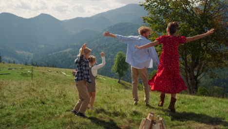 family jumping raising hands up on green hill. parents having fun with children.