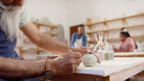 hands of biracial male potter glazing clay jug in pottery studio, slow motion