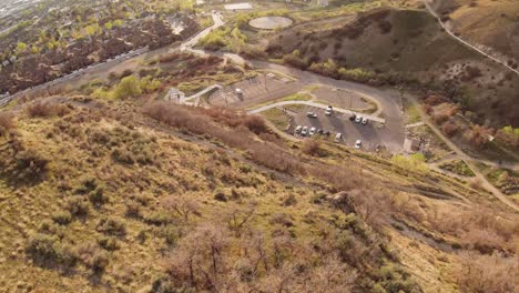 fpv shooting down the steep sunlit mountain illuminated by sun towards the parking lot during sunset