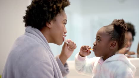 Happy-african-american-mother-and-daughter-brushing-teeth-in-bathroom,-slow-motion