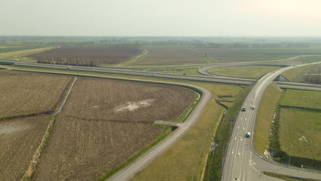 Toma-Aérea-De-Campos-Agrícolas-Al-Lado-De-La-Carretera-Con-Mucho-Tráfico,-Gases-De-Escape-Y-Contaminación-Ambiental