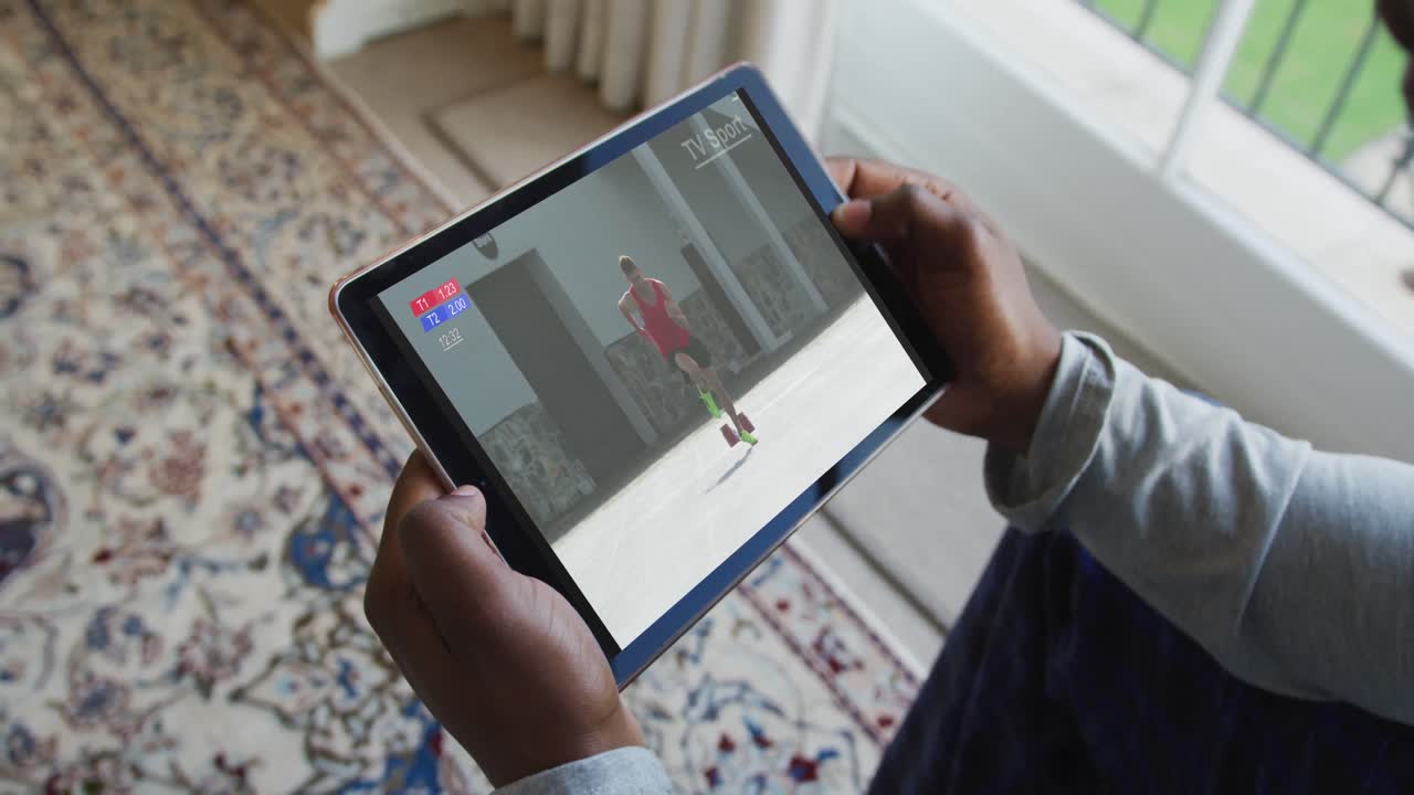 compuesto de un hombre sentado en casa viendo un evento de atletismo en una tableta