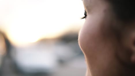 Extremely-close-footage-of-a-female-face,-thoughtfully-looking-to-the-bright,-blurred-percpective.-Brunette.-Smilling