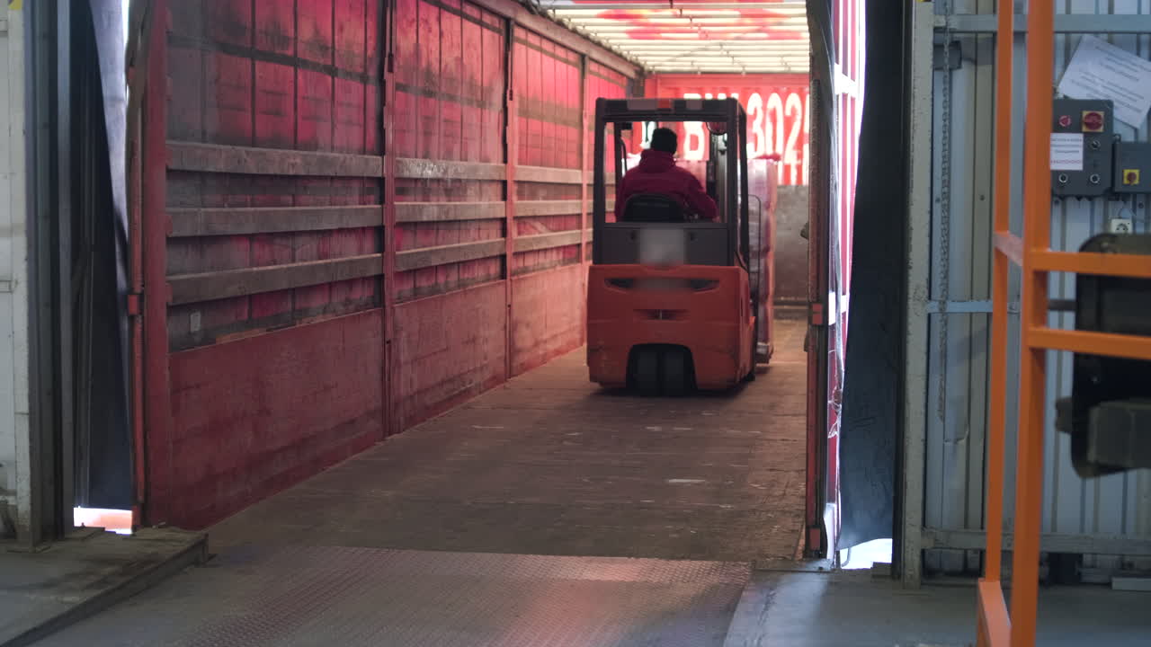 Worker Operating Forklift Loading Pallet into Truck Trailer