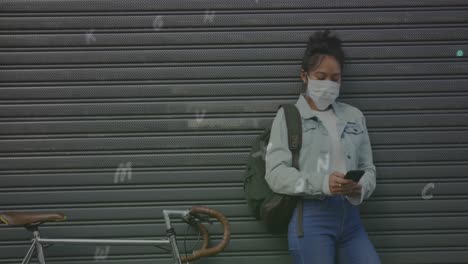 composición digital de múltiples alfabetos que caen contra una mujer que usa una máscara facial usando un teléfono inteligente