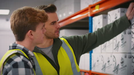 male team leader with digital tablet in warehouse training intern standing by shelves