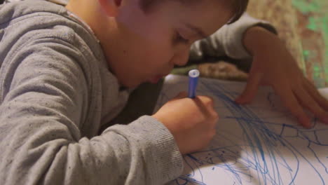 caucasian toddler boy draws with colour markers on paper zoom in