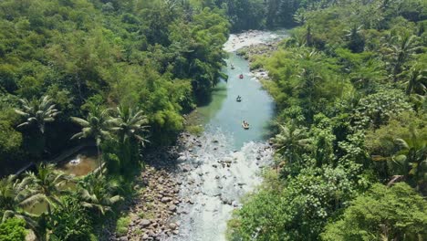 Drone-view-turquoise-river-surrounded-by-green-trees-crossed-by-rafting-boats