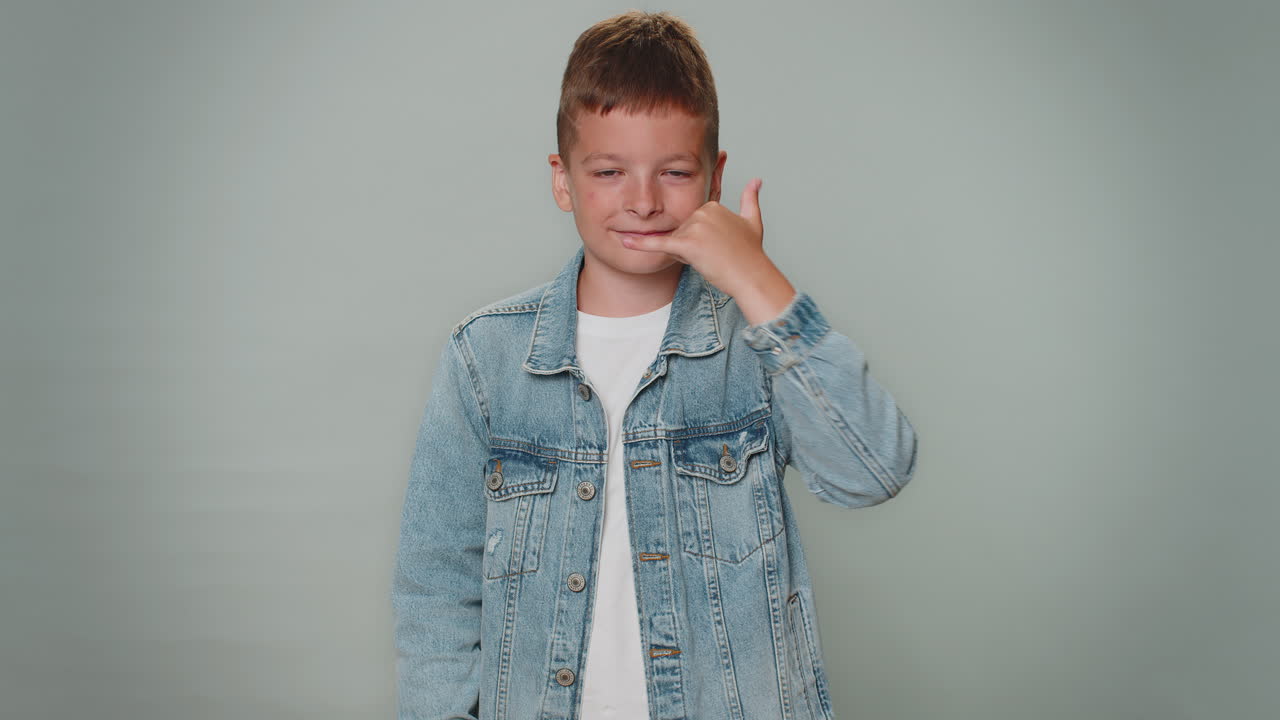 маленький мальчик смотрит в камеру, делая телефонный жест, как говорит: "привет, вы мне перезвоните, номер контакта".
