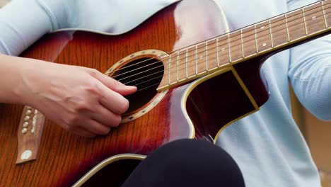 una joven de primer plano toca la guitarra cerca de una casa antigua