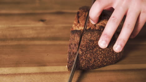 primer plano estático de un pan de masa madre sabroso, crujiente, delicioso y recién horneado que un hombre caucásico corta en una tabla de cortar de madera